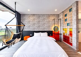 Habitación de hotel con una cama grande, una hamaca, vistas a la ciudad y una pared colorida.