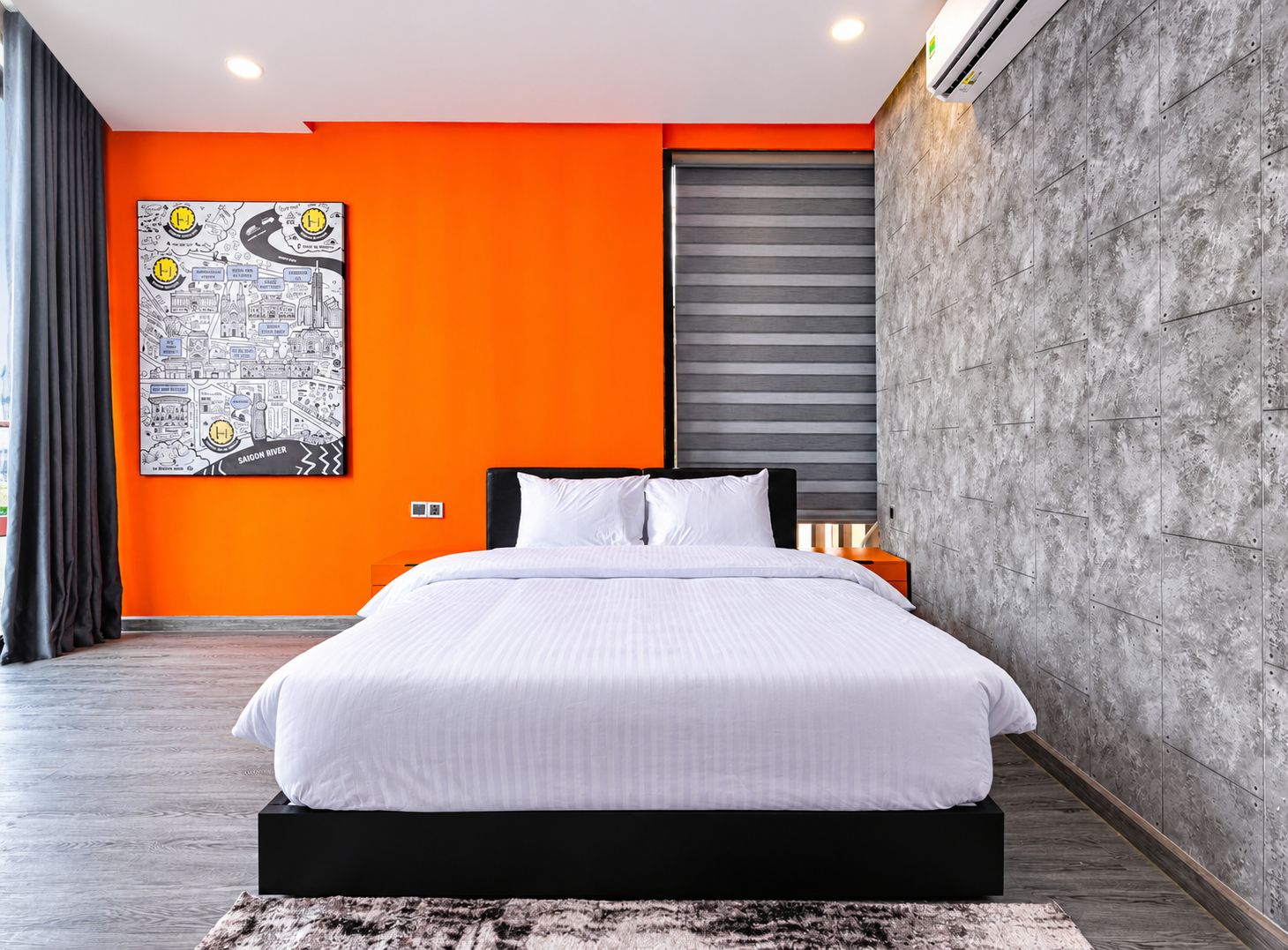Un dormitorio moderno con una cama grande, una pared de acento naranja, una obra de arte con un paisaje urbano y una pared texturizada gris.