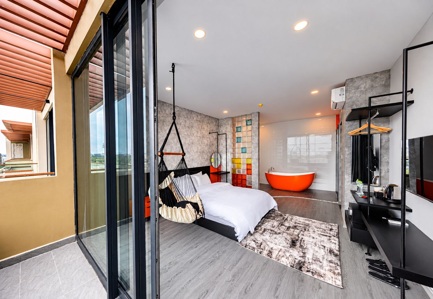 A modern bedroom with a large bed, a hanging chair, a bathtub, and a glass door leading to a balcony.