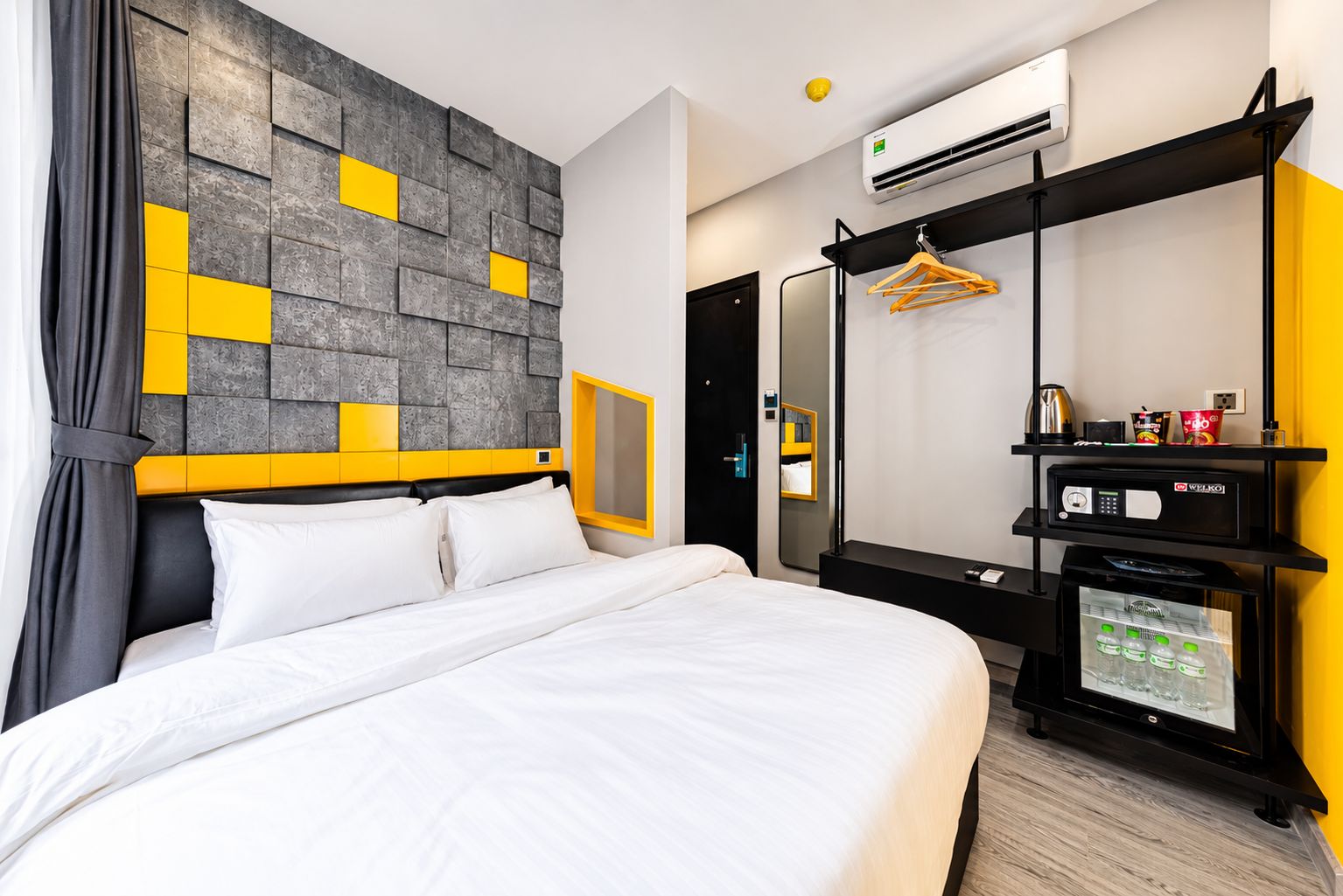 A hotel room with a bed, a wardrobe, a minibar, and a wall-mounted air conditioner.