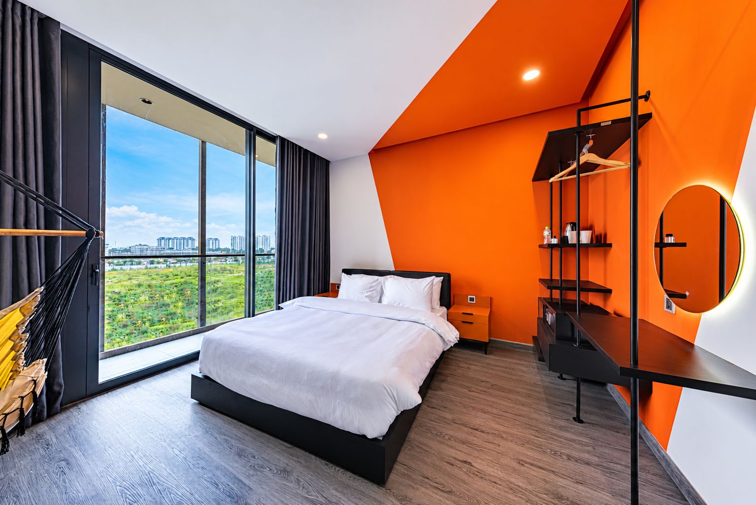 Un dormitorio moderno con una cama grande, vista a la ciudad y una pared de acento naranja singular.