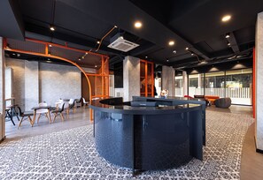 A modern interior with a central black table, seating area with chairs, and a staircase with orange railings.