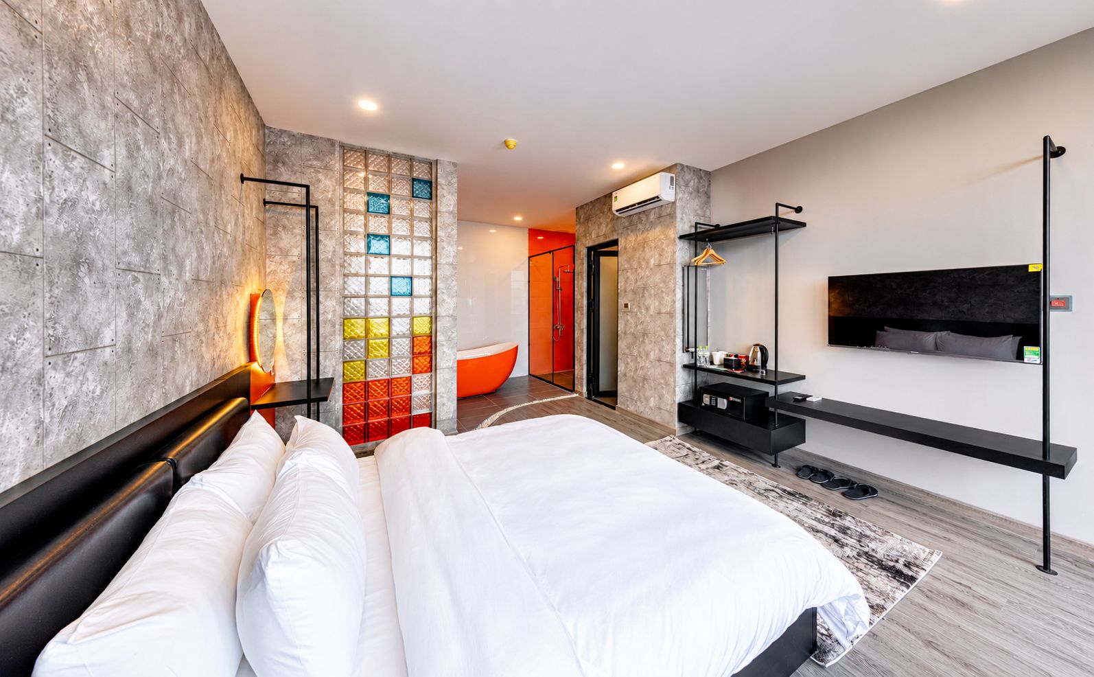 Una habitación de hotel moderna con una cama grande, un televisor montado en la pared y un banco empotrado con espacio de almacenamiento.
