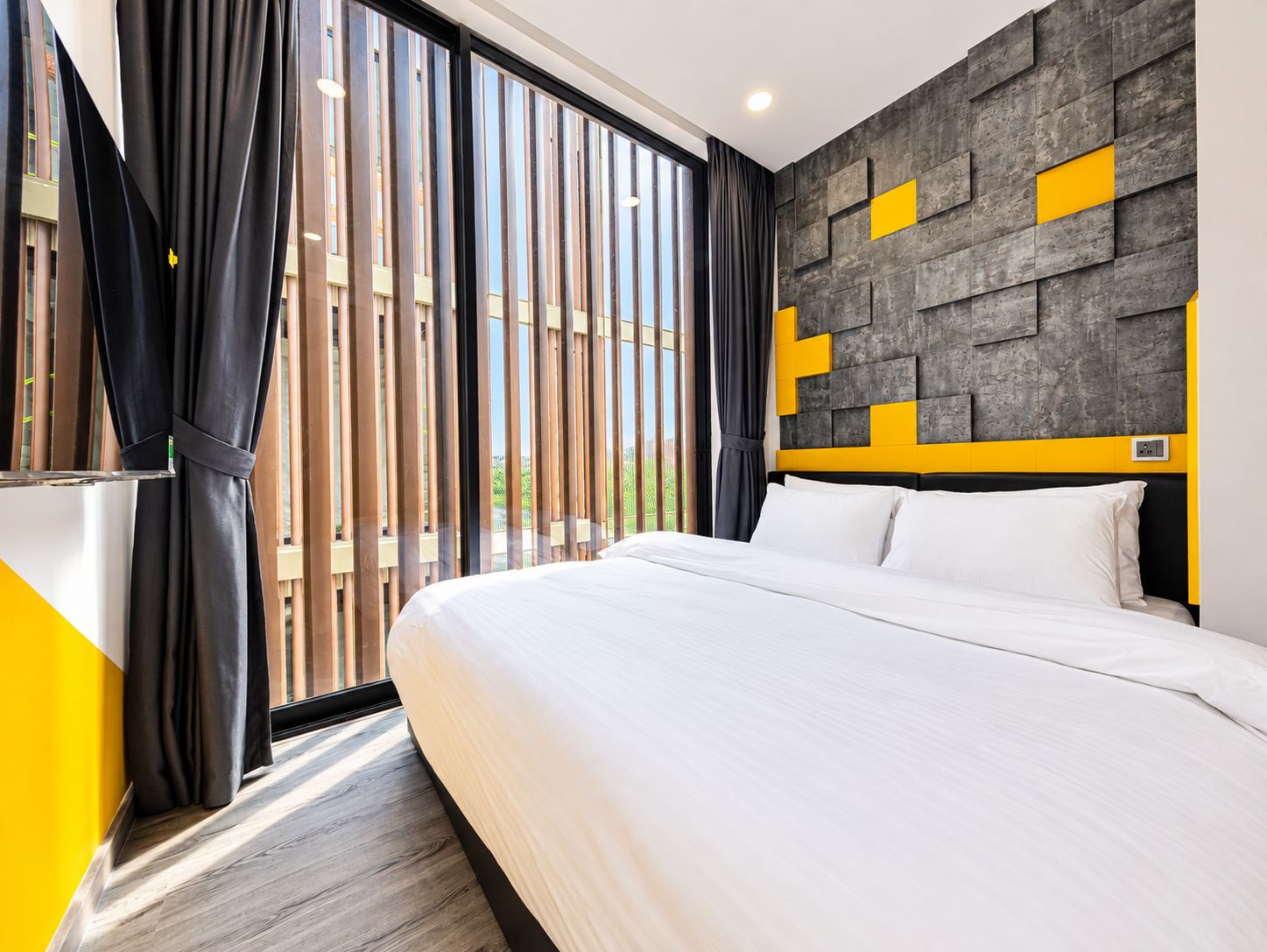 Una habitación de hotel moderna con una cama grande, vistas a través de ventanales del suelo al techo y un diseño de pared original con patrones geométricos.