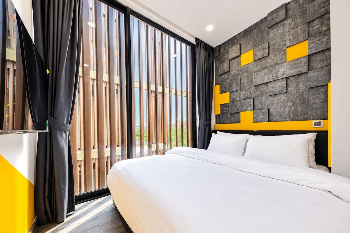 A modern hotel room with a large bed, a view through floor-to-ceiling windows, and a unique wall design with geometric patterns.