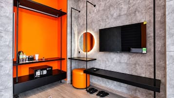 Un baño moderno con pared de azulejos grises, un estante negro con artículos de aseo, un espejo redondo con luz y un banco negro.