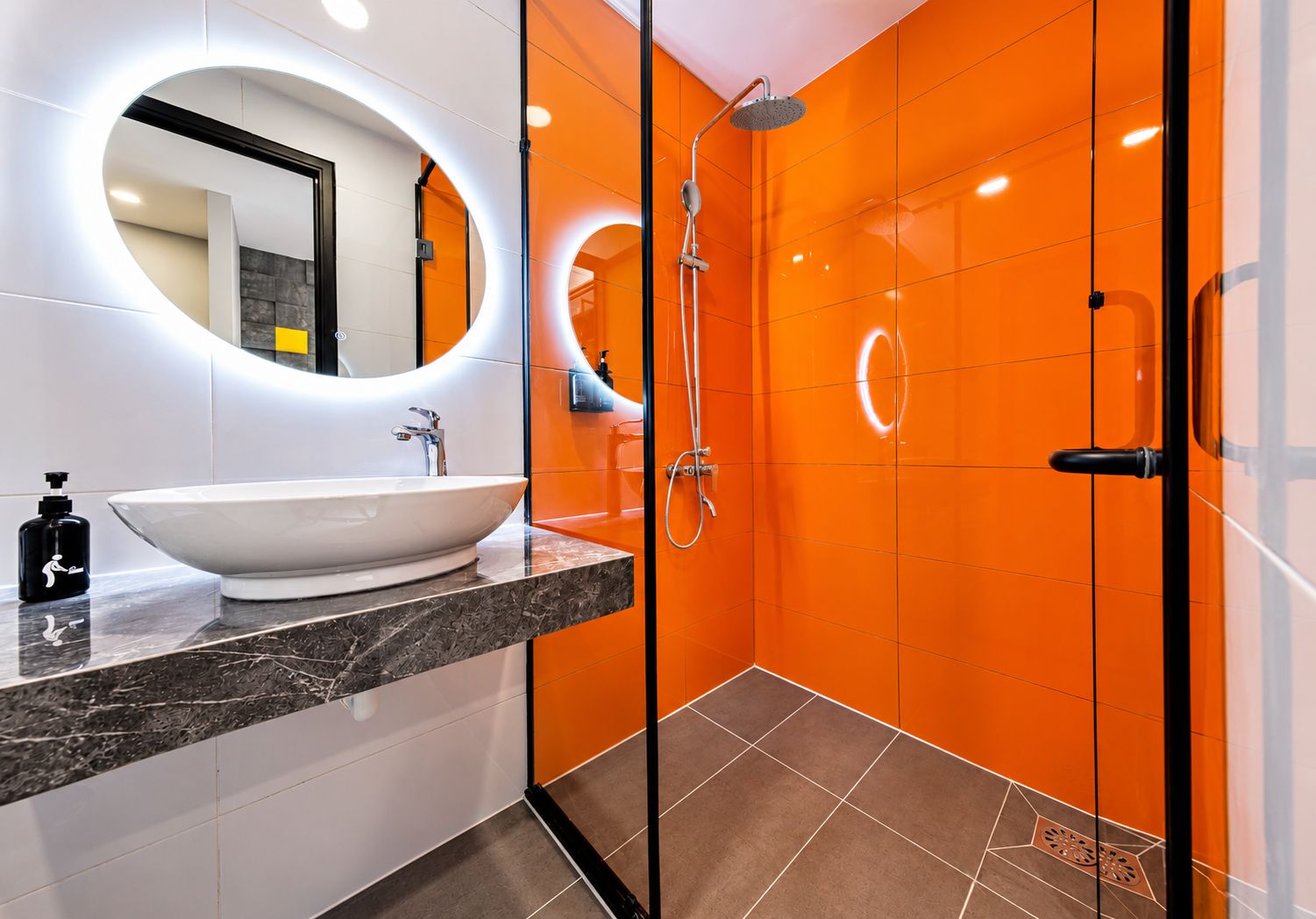 Un baño moderno con un lavamanos blanco, un cabezal de ducha de mano y una ducha con mampara de vidrio.