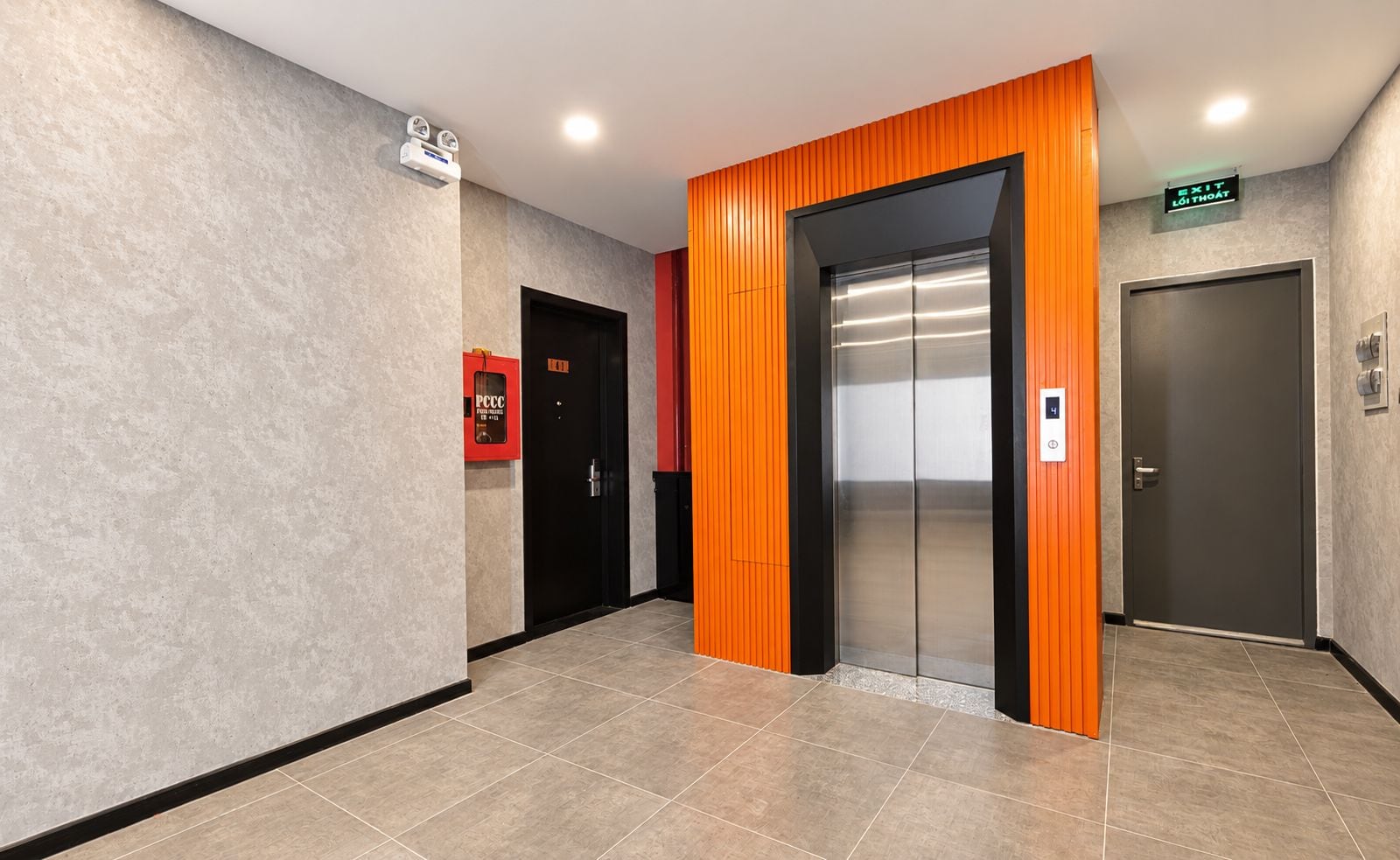 Un ascensor moderno con detalles metálicos, una caja de alarma contra incendios y una puerta con un letrero que indica una salida.