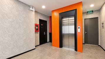 Un ascensor moderno con detalles metálicos, una caja de alarma contra incendios y una puerta con un letrero que indica una salida.