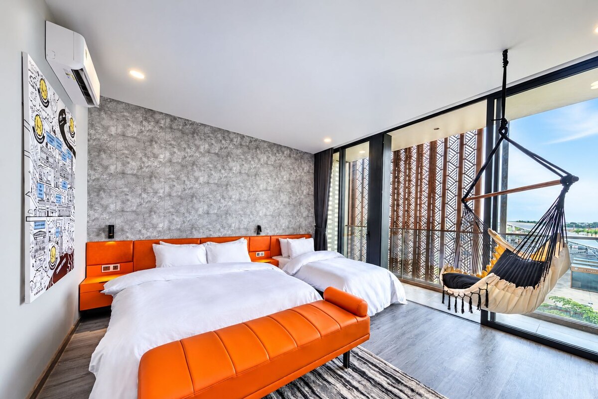 A modern bedroom with a large bed, a hammock, and a cityscape view.