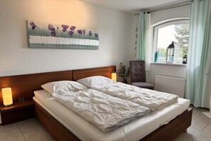 A bedroom with a bed, a nightstand, a chair, a window with curtains, and a wall-mounted painting. - Residence Juliana 68 (Julianadorp aan Zee)