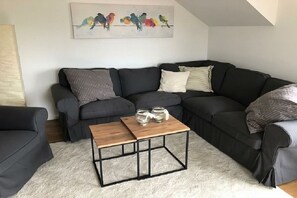 A modern living room with a sectional sofa, a coffee table, and a painting of birds on the wall. - Holiday apartment with 1 bedroom (Fehmarn)