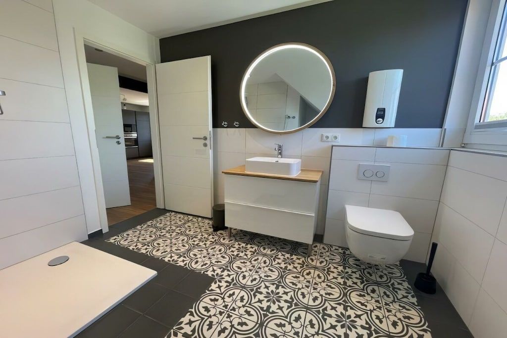 Un bagno moderno con pavimento decorato, uno specchio rotondo, un water e un lavandino.