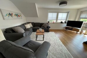 A modern living room with a sectional sofa, a coffee table, a flat-screen TV, and a painting of birds on the wall. - Holiday apartment with 1 bedroom (Fehmarn)