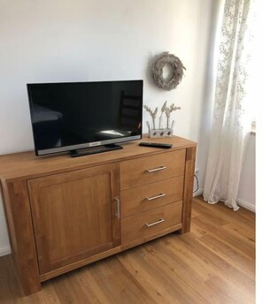 A wooden TV stand with a flat-screen TV, a remote control, and decorative items. - Holiday apartment with 1 bedroom (Fehmarn)