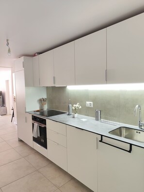A modern kitchen with white cabinets, a stainless steel sink, and a built-in oven.