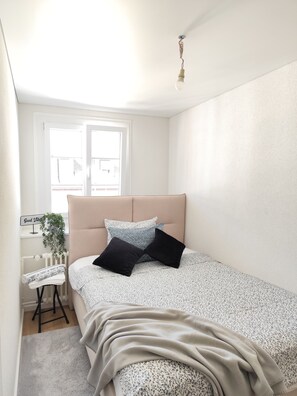 Et soveværelse med seng, sengebord, radiator, vindue og en hængende lampe.