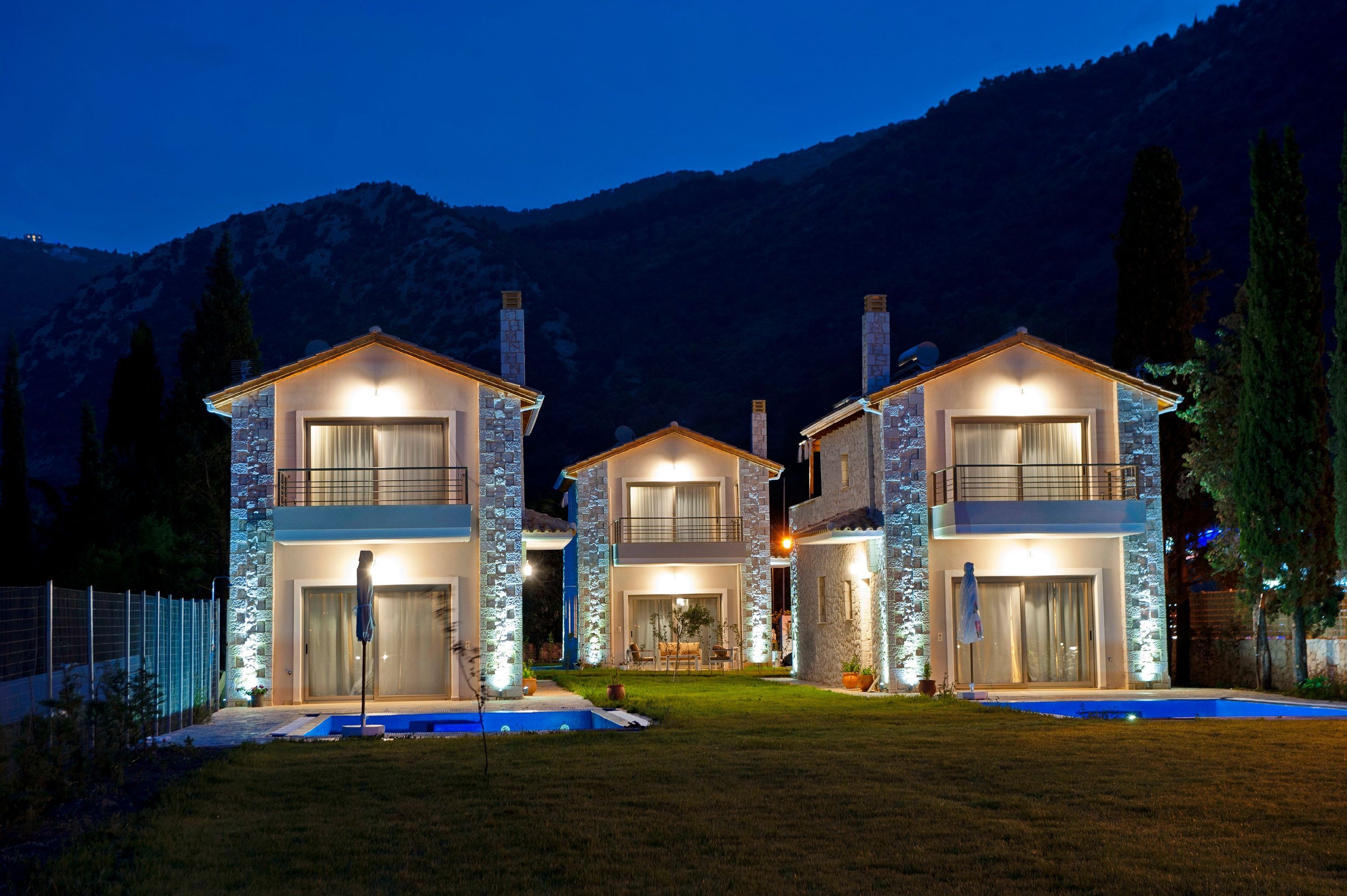 Une maison à trois étages avec une piscine à l’avant, entourée d’une clôture et d’arbres.