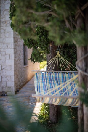 A hammock hanging from a tree in a courtyard with stone walls and a pathway. - Avesta Private Villas Niovi (Lefkada)