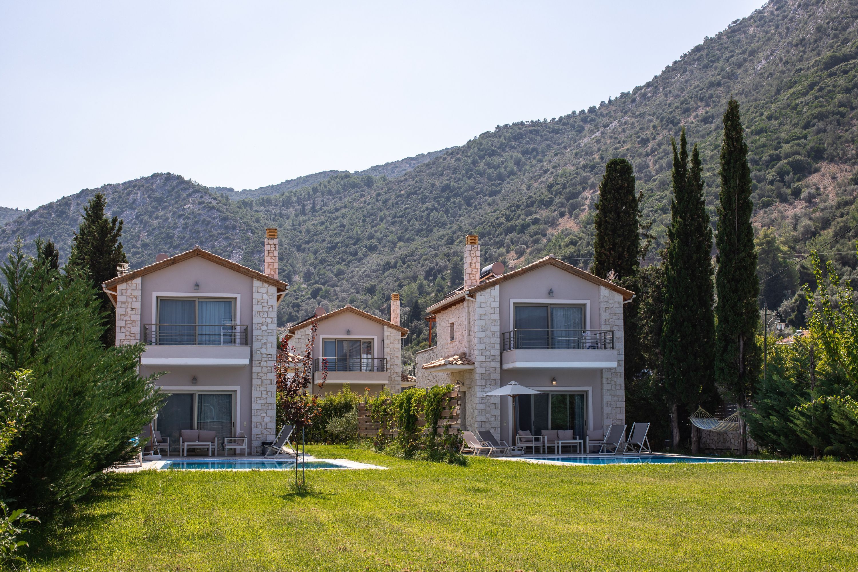 A two-story building with a pool, surrounded by greenery and mountains.