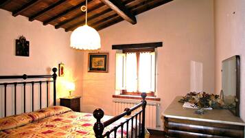 Une chambre à coucher comprenant un lit, une table de chevet, une commode, une fenêtre avec des rideaux et un luminaire suspendu.