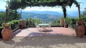 Un patio exterior con una mesa y sillas, rodeado por una pérgola y plantas en macetas.