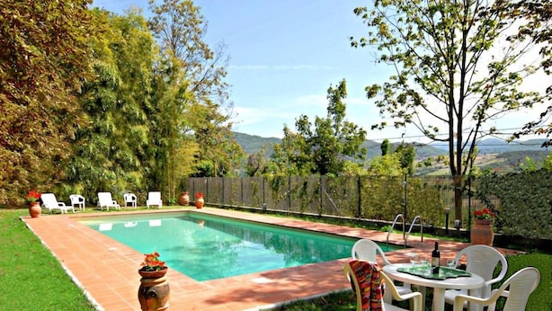 Piscina con zona de terraza, rodeada de vegetación y vistas a colinas.