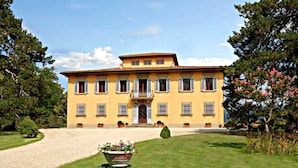 Un edificio grande y amarillo con fachada simétrica, varias ventanas con contraventanas y una entrada central con puerta.