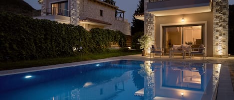 A modern two-story house with a swimming pool, stone exterior, and outdoor seating area.