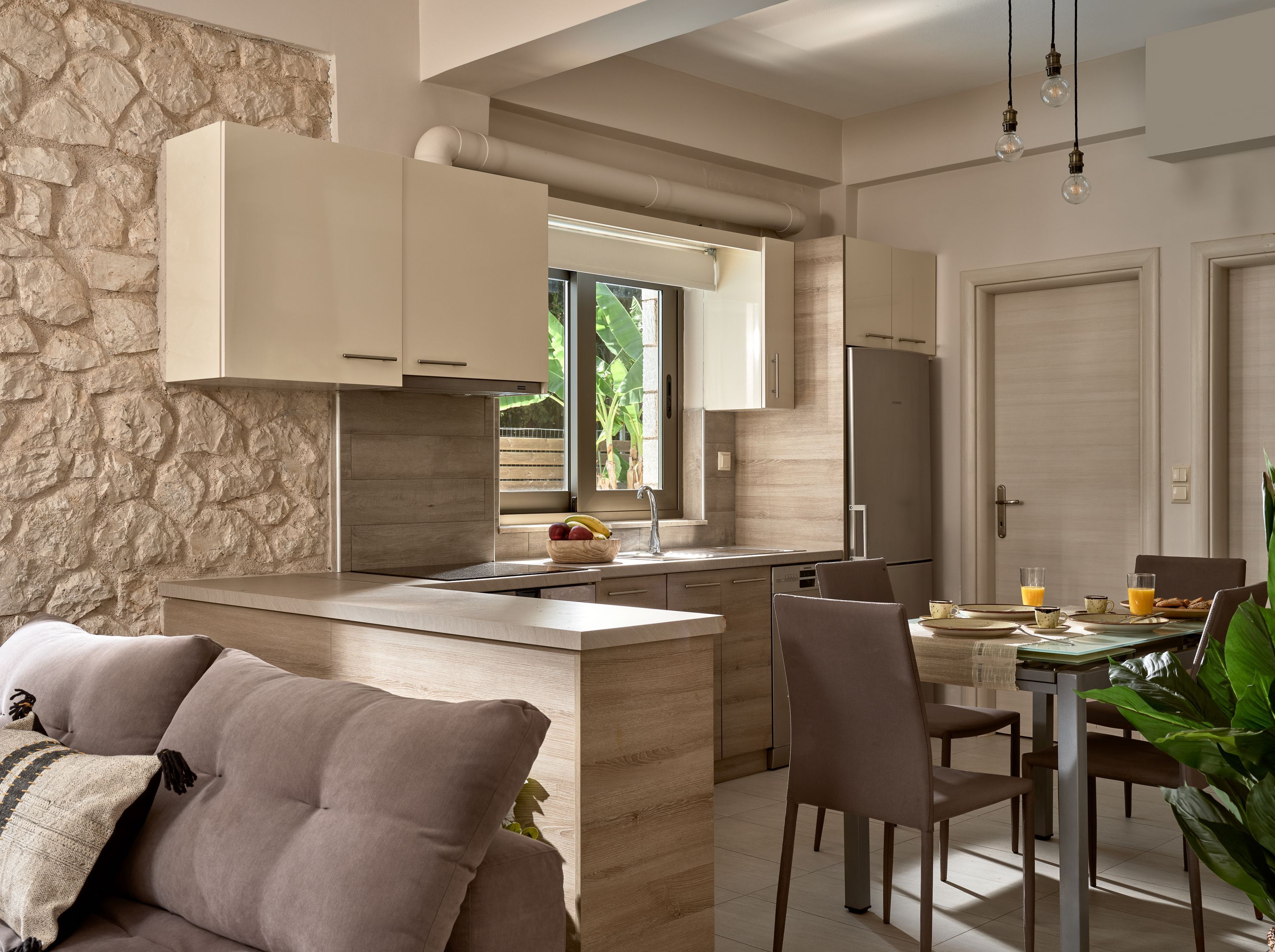 Cozinha moderna com parede de pedra, área de jantar com mesa e cadeiras e uma geladeira.