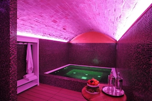 A room with a hot tub, pink lighting, and a fruit bowl on a table. - Relais San Giovanni (San Giovanni In Marignano)