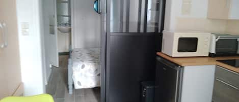 Una cocina funcional con refrigerador, microondas y un pequeño basurero.