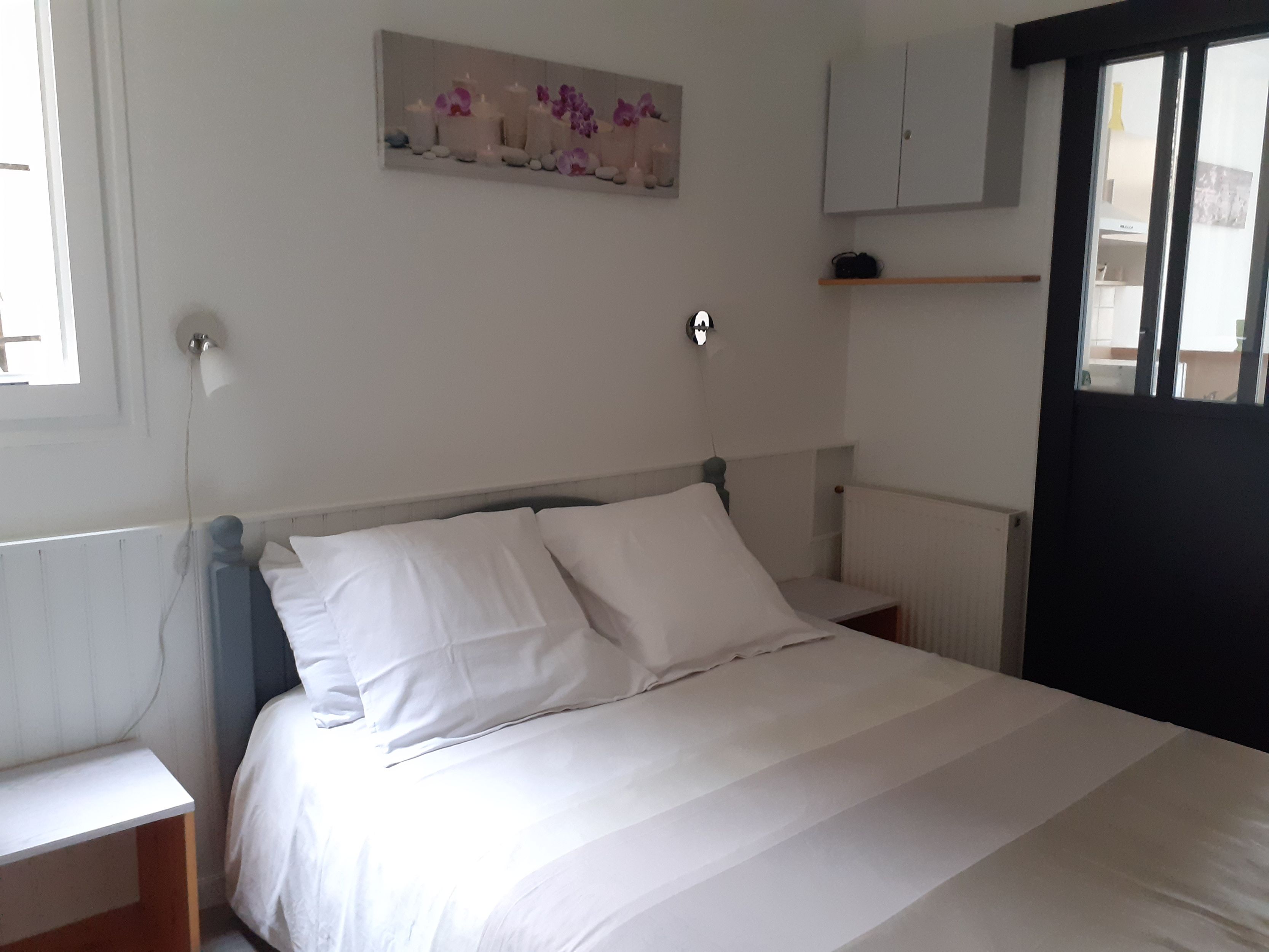 A bedroom with a bed, nightstands, a wall-mounted shelf, and a window.