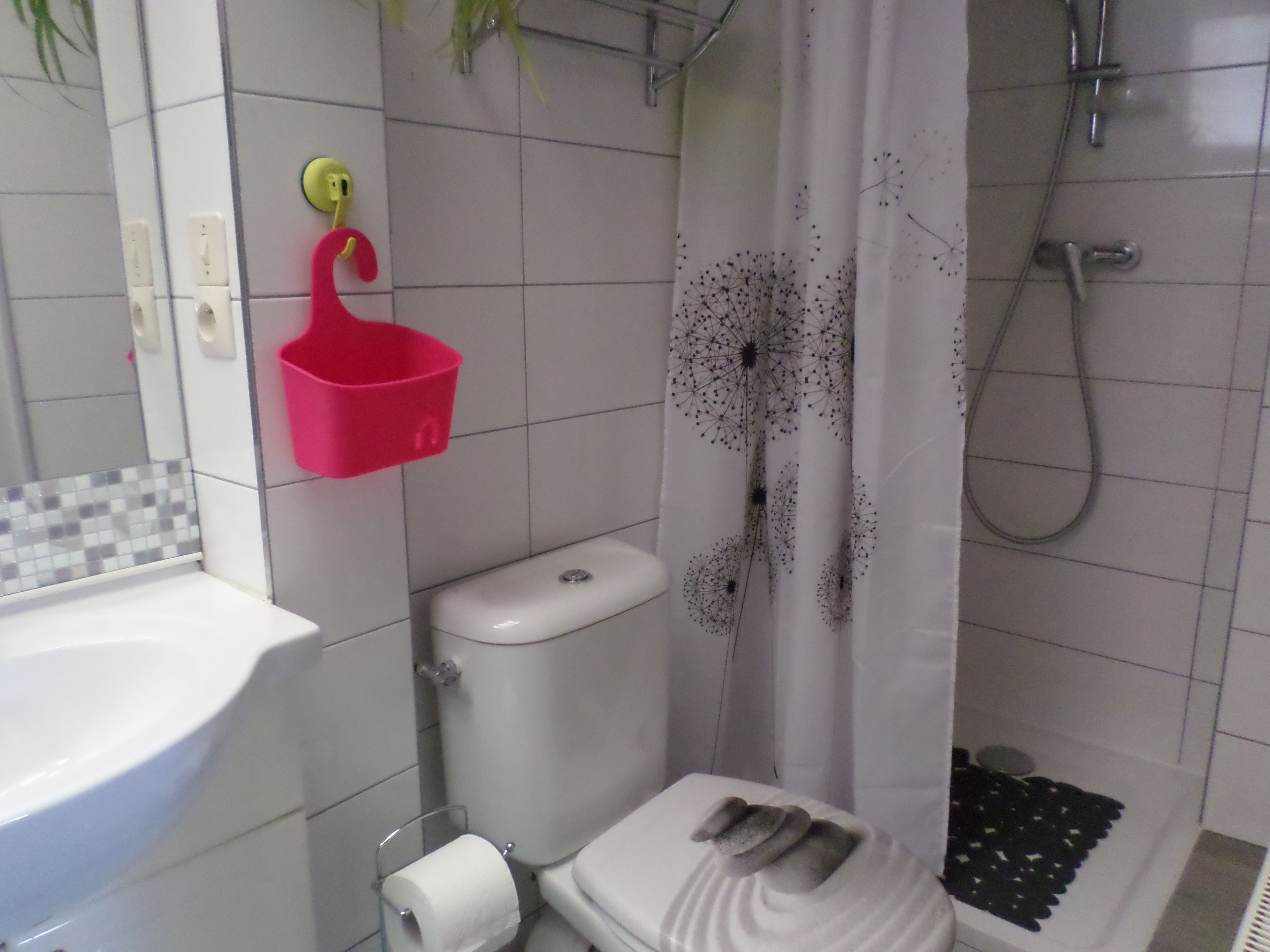 A bathroom with a toilet, sink, shower, and a pink basket on the wall.
