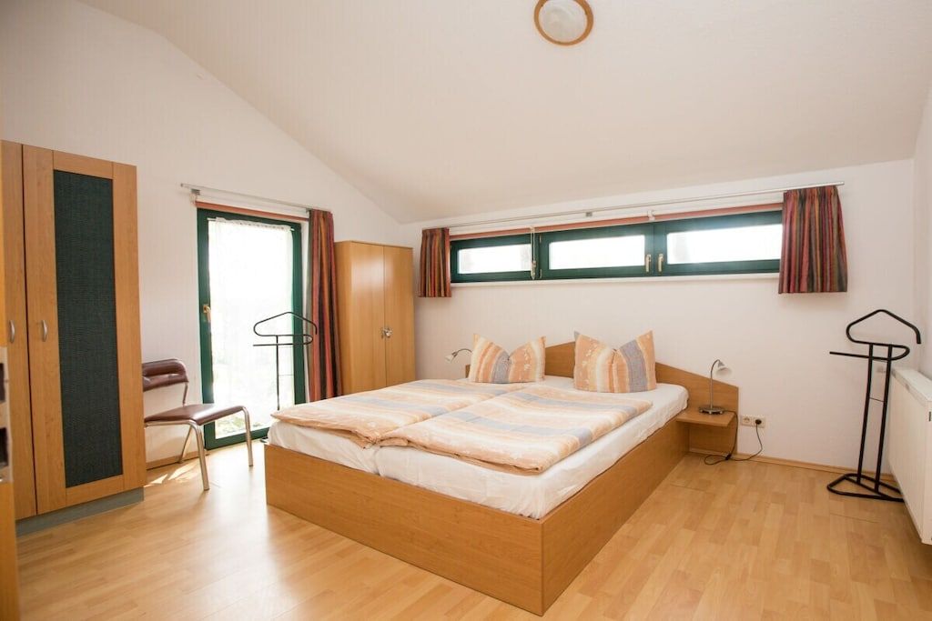A bedroom with a wooden bed, a chair, a wardrobe, and a window with curtains.
