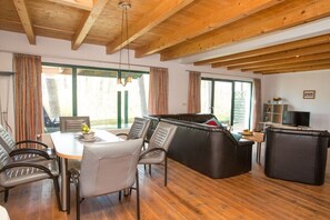 A spacious living area with a wooden ceiling, a dining table with chairs, a sofa, and a television on a stand. - Holiday home Waldschneise A at Jabeler See (Jabel)