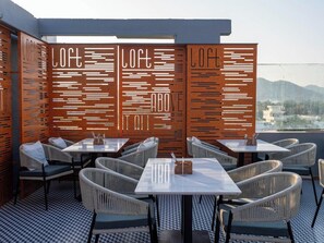 Un espace extérieur aménagé avec des tables et des chaises, un mur décoratif orné de motifs et une vue sur le paysage.