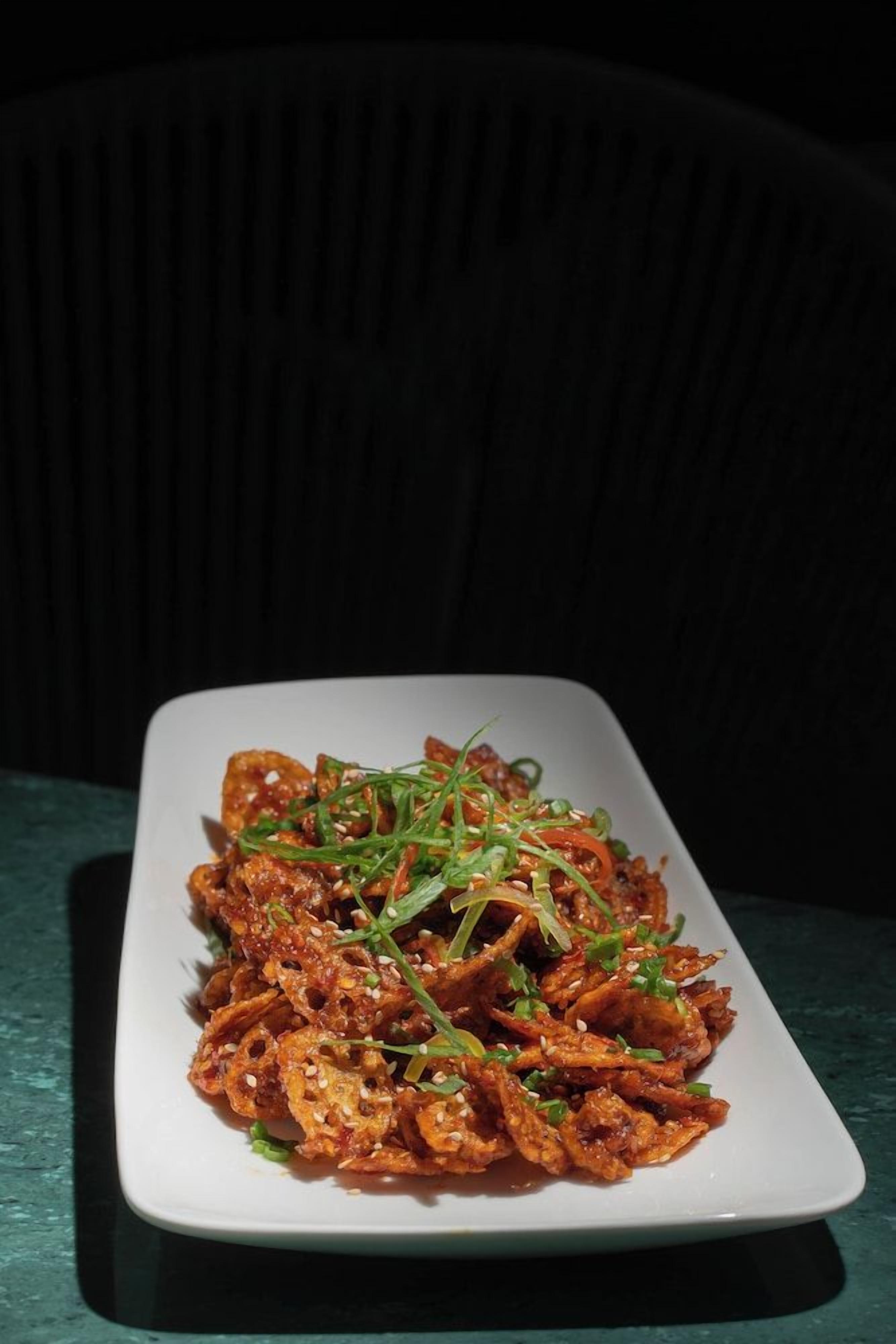 A rectangular white plate with a dish of food garnished with green herbs and sesame seeds, placed on a dark surface.