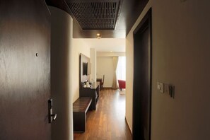 A hallway with a bench, a door, and a red chair in the distance. - Hotel Mumbai House (Udaipur)