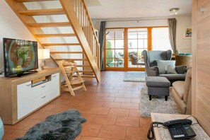 Ein Wohnzimmer mit Holzboden, einer Treppe, einem Fernseher, einer Couch und einem Telefon.