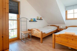 Ein Schlafzimmer mit zwei hölzernen Betten, einem Metallregal mit Büchern, einer Holzleiter und einem Fenster mit Jalousien.