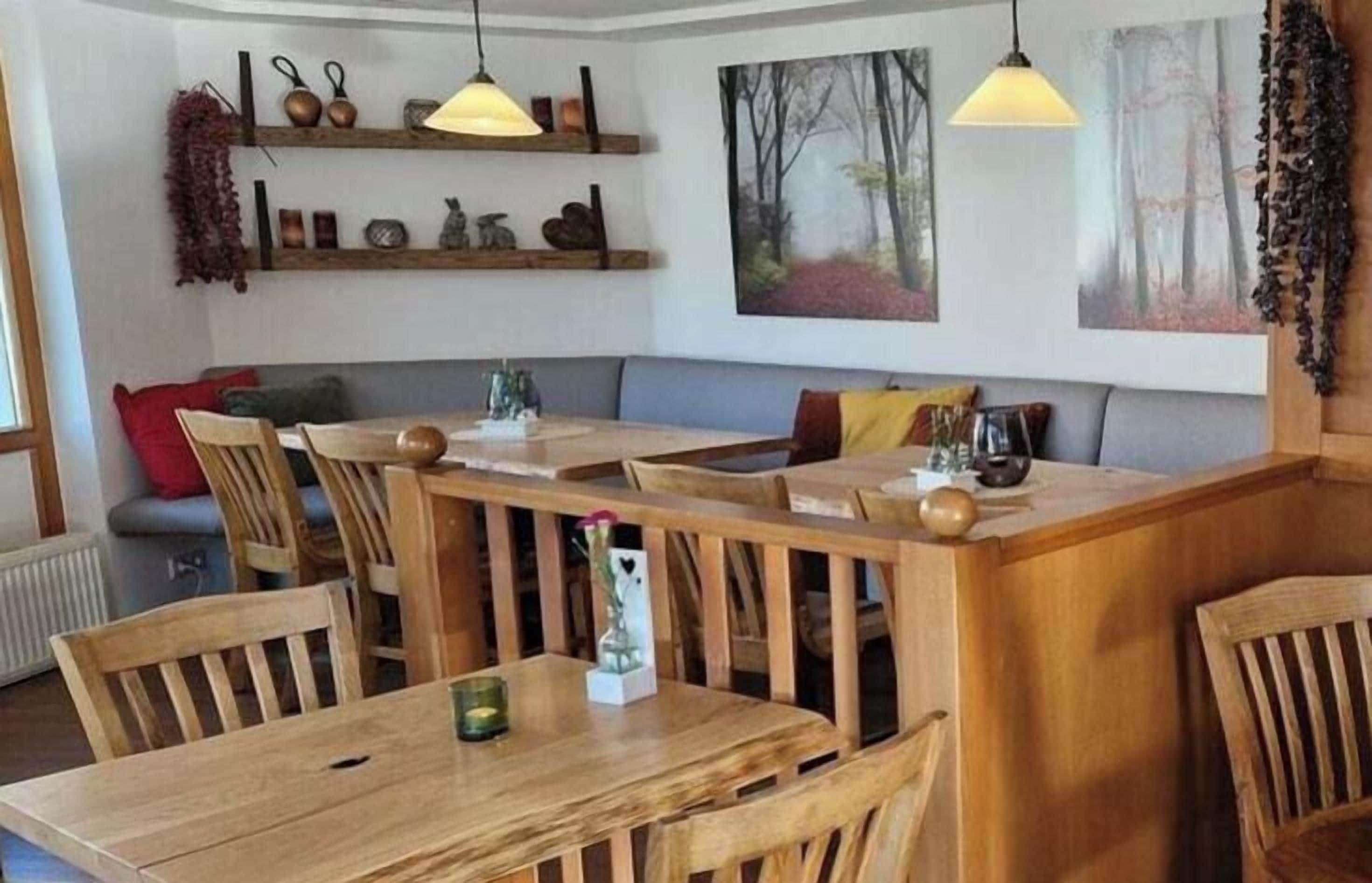 Un comedor con mesas y sillas de madera, un banco e iluminación colgante.