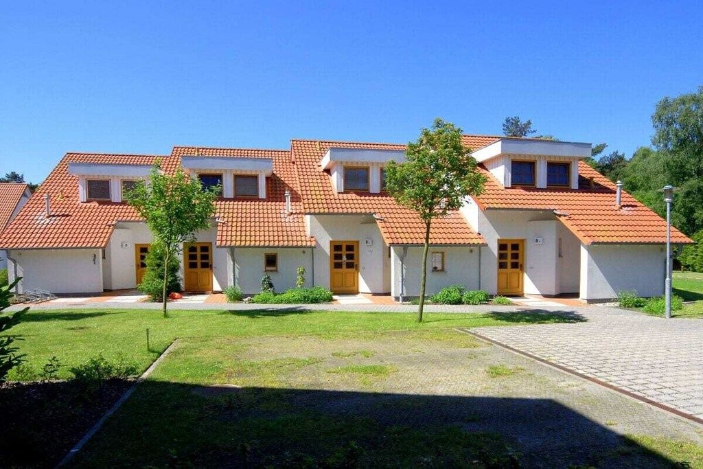 A row of white buildings with red-tiled roofs, a paved driveway, and small trees in front.