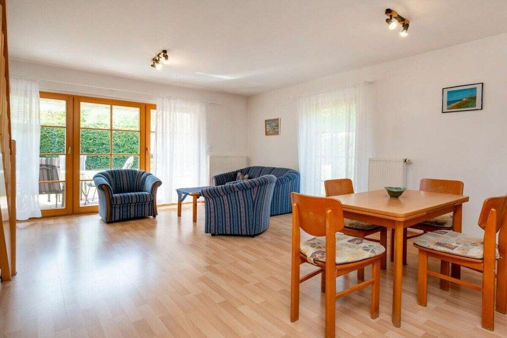 A spacious room with a wooden dining table, four chairs, a sofa, and two armchairs.