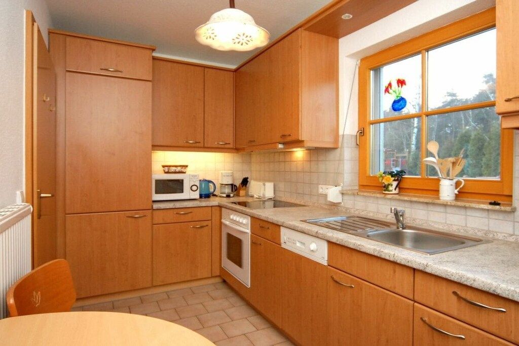 Une cuisine avec des meubles en bois, un four à micro-ondes, un four traditionnel, un évier et une fenêtre donnant sur un paysage verdoyant.
