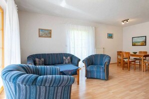 A living room with a sofa, armchair, and dining table with chairs. - 8c/T5 holiday home park “Freesenbruch” (Zingst (Ostseeheilbad))
