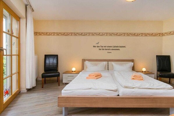 A hotel room with a double bed, two bedside tables, a chair, and a decorative wall quote. - 1.3/T2 holiday home park “Freesenbruch” (Zingst (Ostseeheilbad))