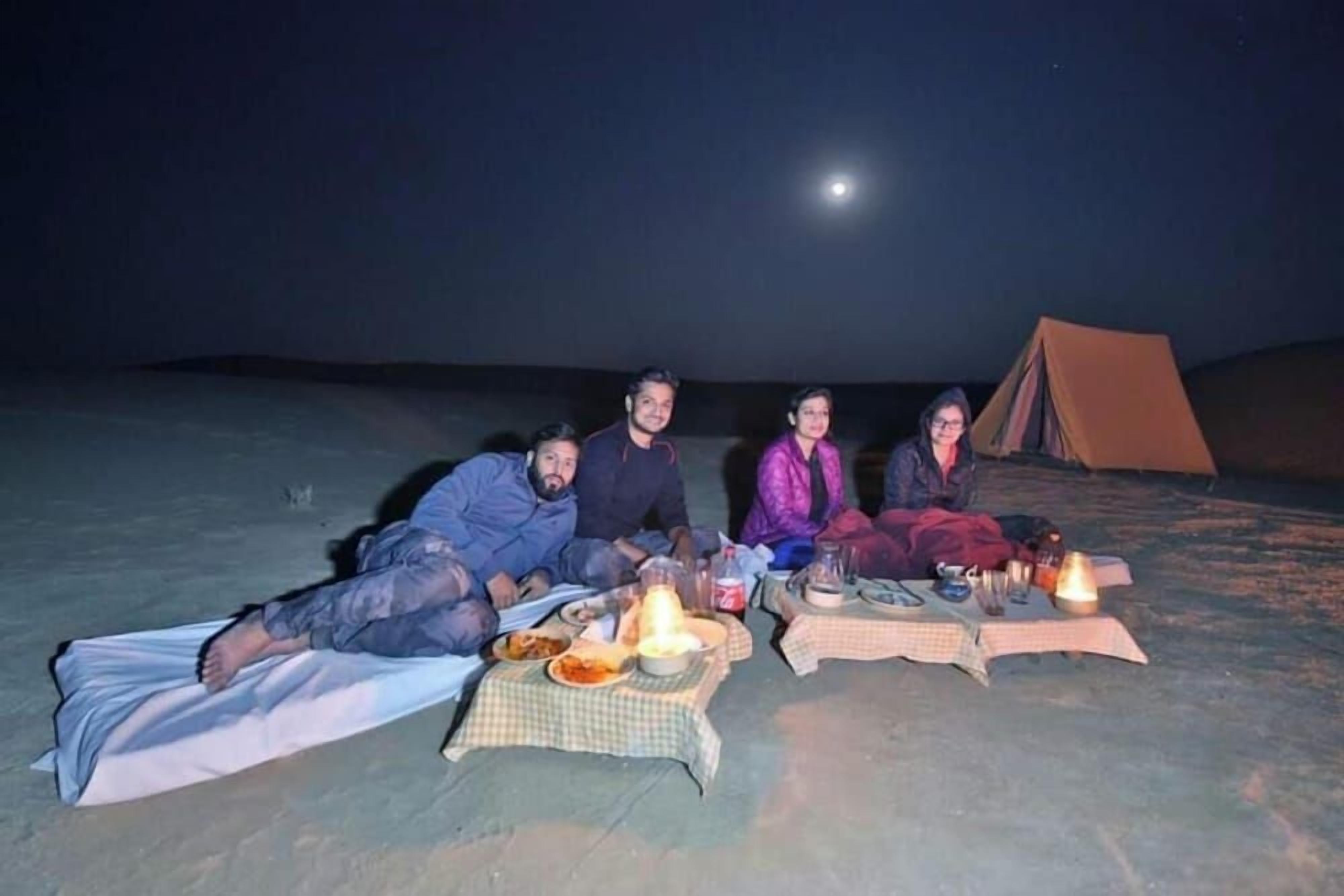 A group of people sitting on the ground with a tent in the background.