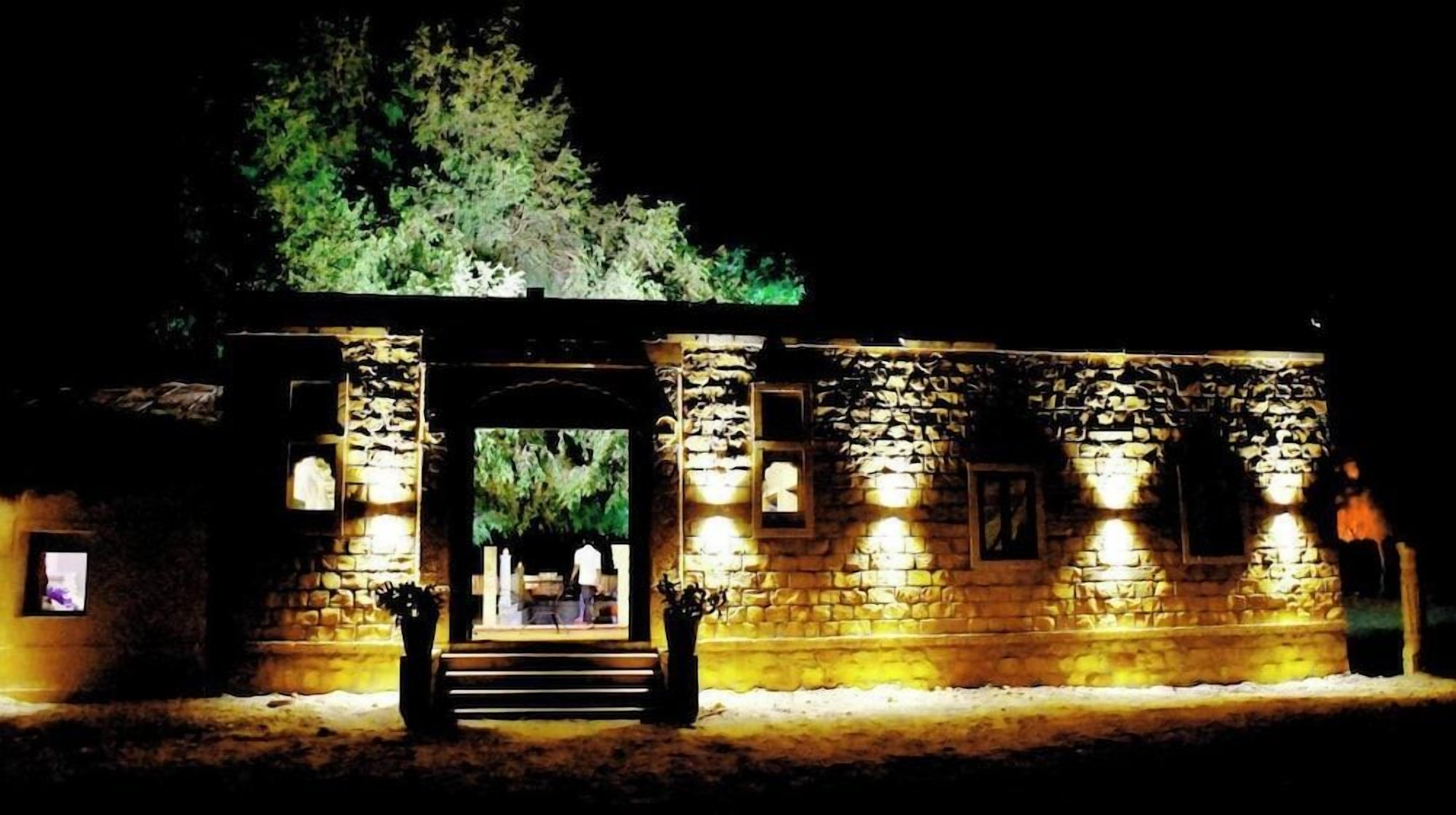 A stone building with a central archway, illuminated by exterior lights, and a staircase leading to an upper level.