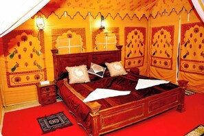 A room with a bed, pillows, a nightstand, and a lamp. - The Chirag Desert Camp (Jaisalmer)